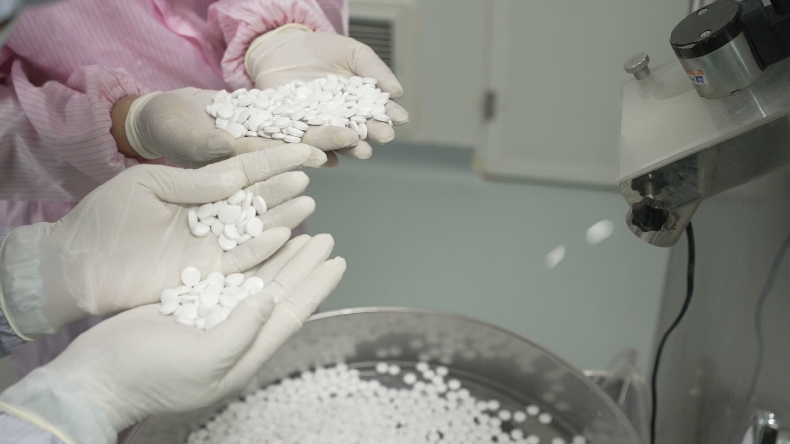Gloved operators holding white tablet-shaped units beside production equipment